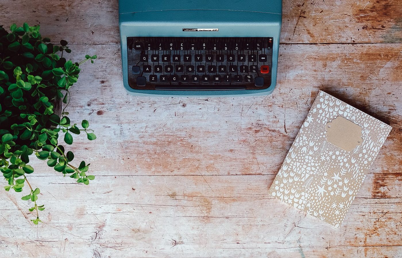 Machine à écrire turquoise et carnet posés sur une table en bois clair