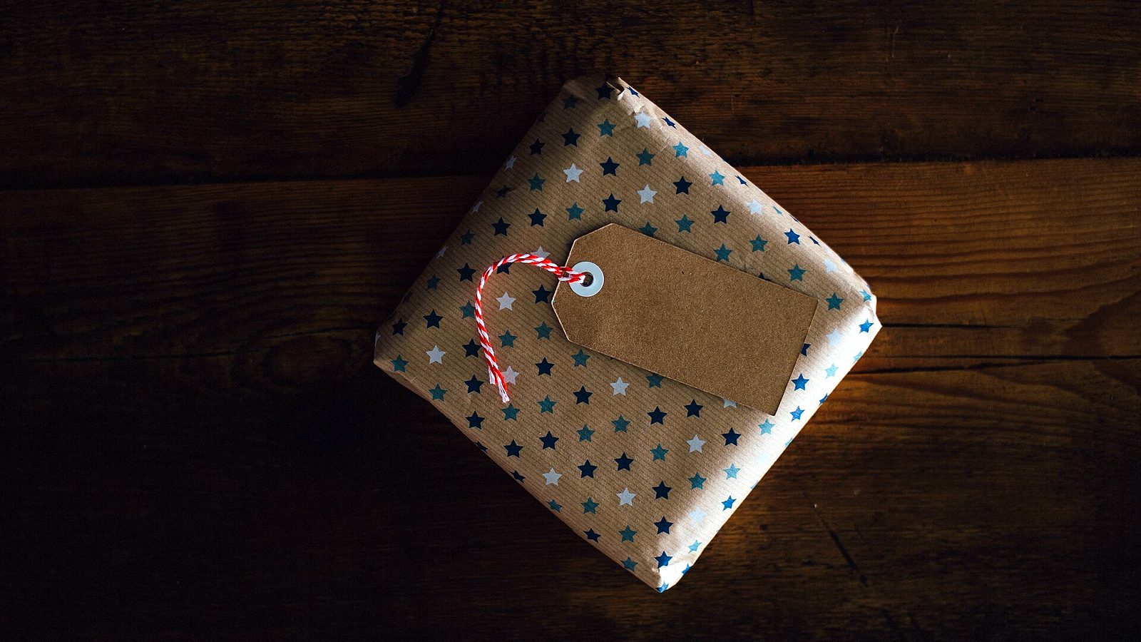Paquet cadeau emballé de papier à étoiles, posé sur un plancher sombre